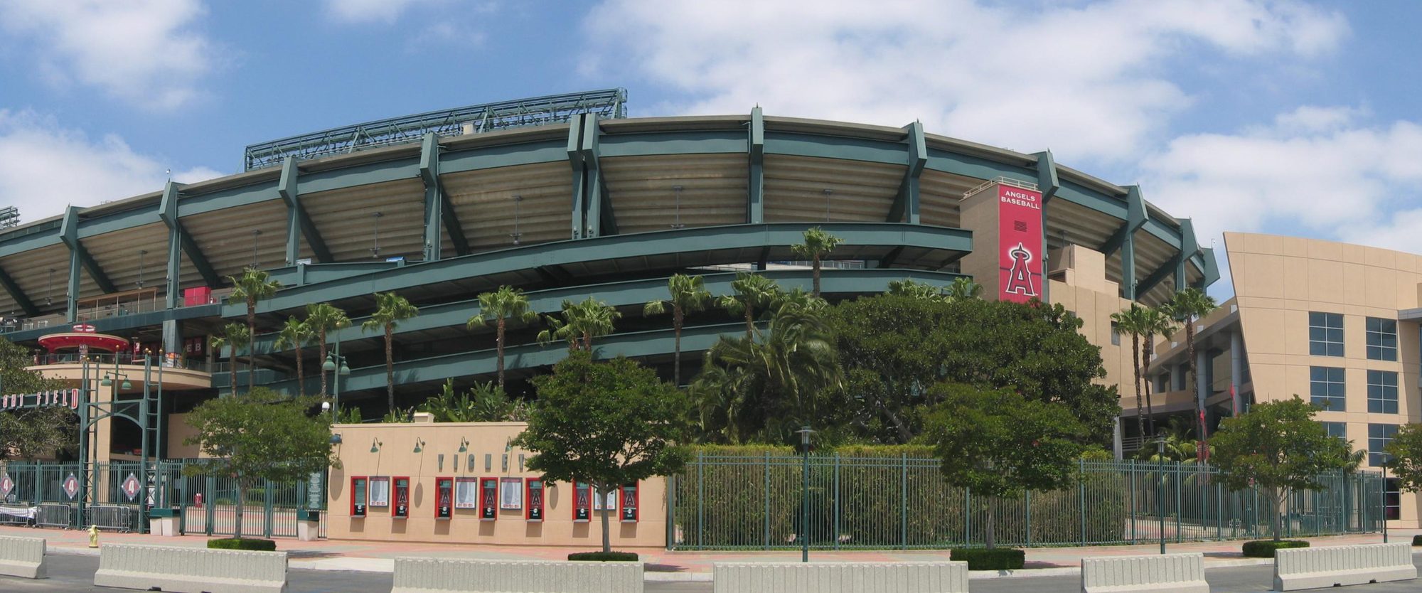 The exterior of Angel Stadium in Anaheim, its curved upper deck rising above the palm trees along the entrance plaza