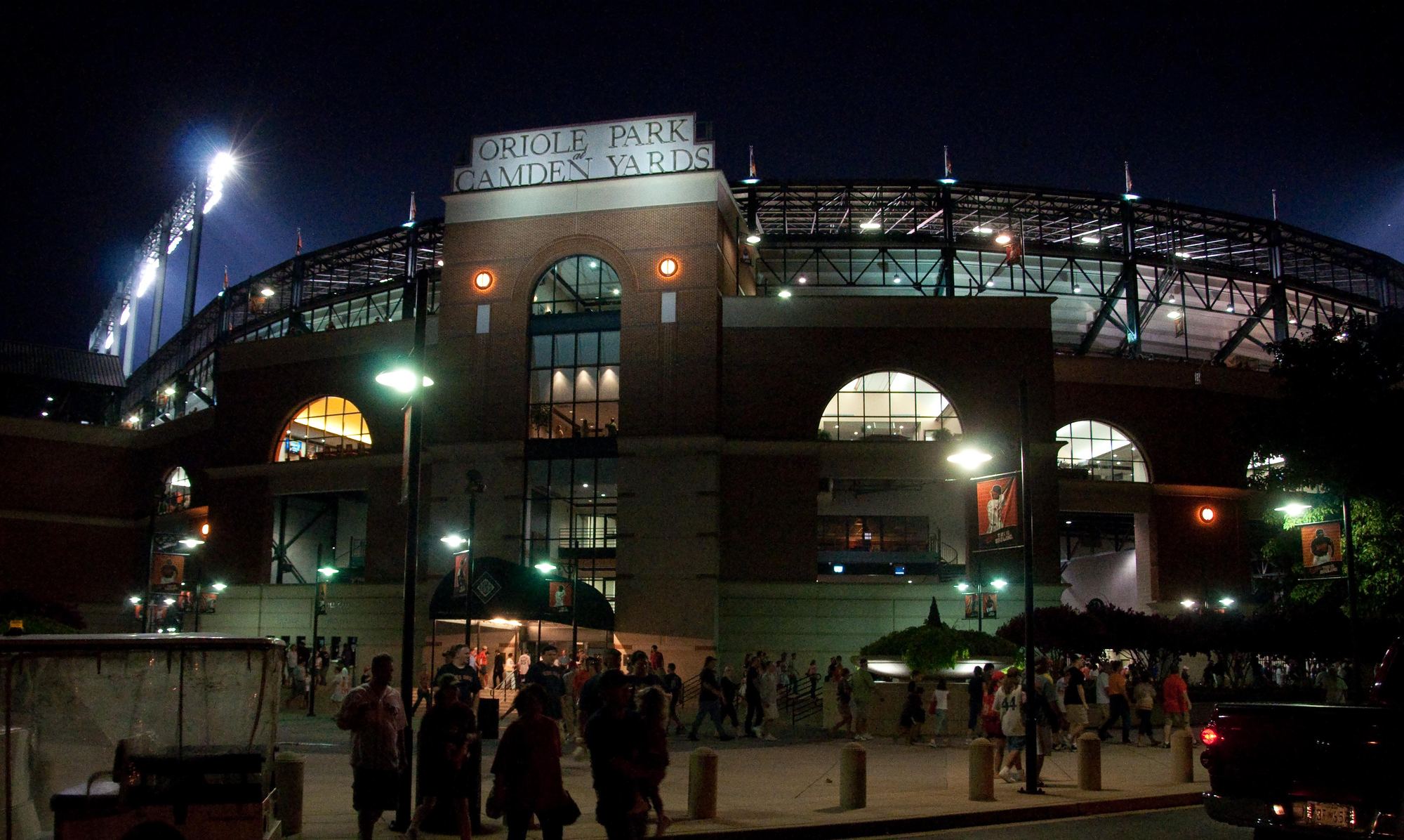 The main gate at Oriole Park at Camden Yards at night, with fans heading inside under the lights