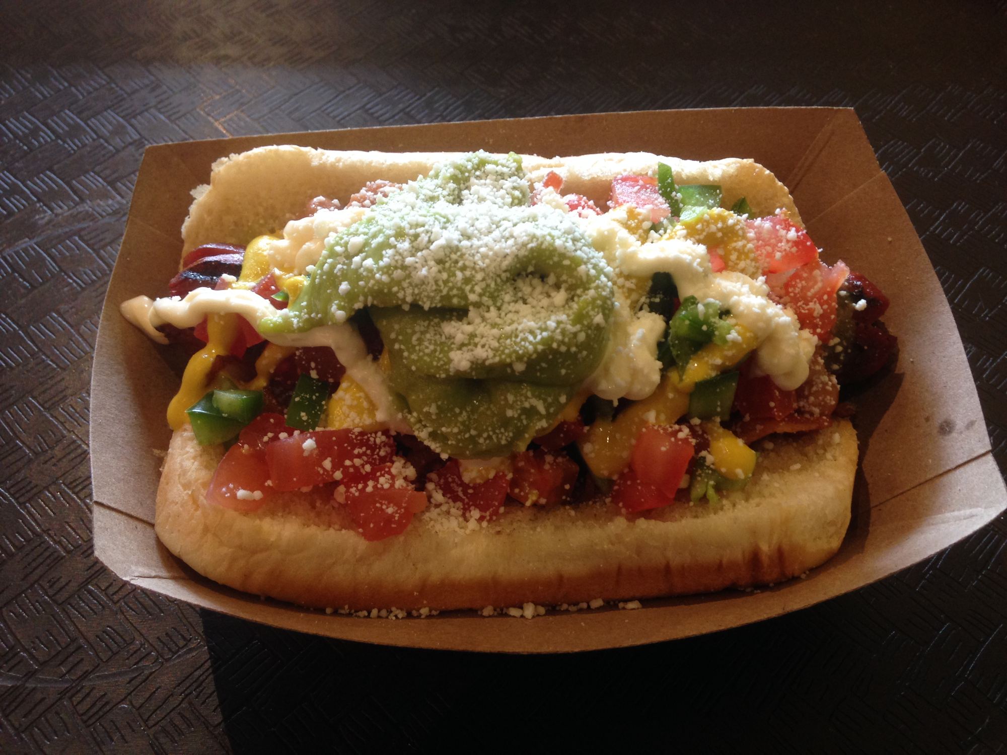 A Sonoran hot dog loaded with toppings in a paper tray