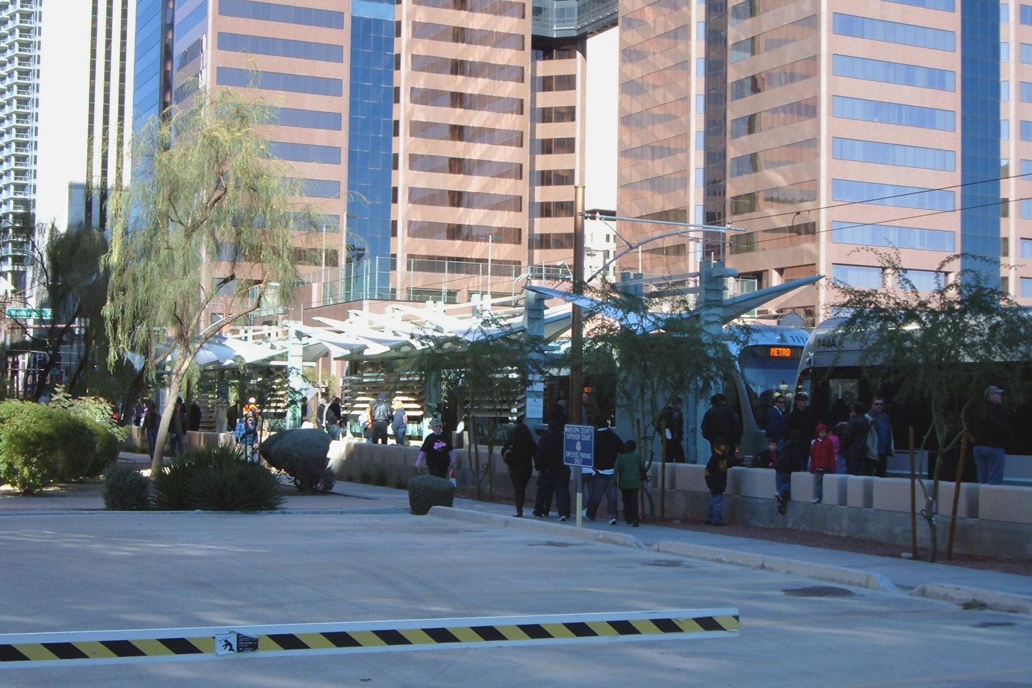 A Valley Metro light rail train at a downtown Phoenix platform, with riders walking toward it and the downtown office towers behind