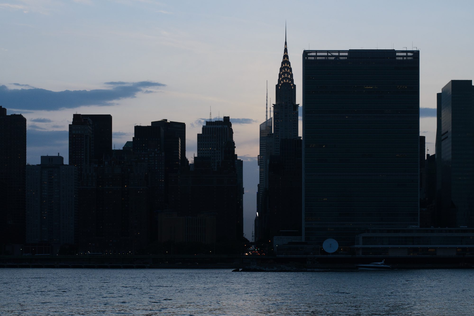 The Midtown Manhattan skyline in silhouette at dusk, seen across the East River from Queens