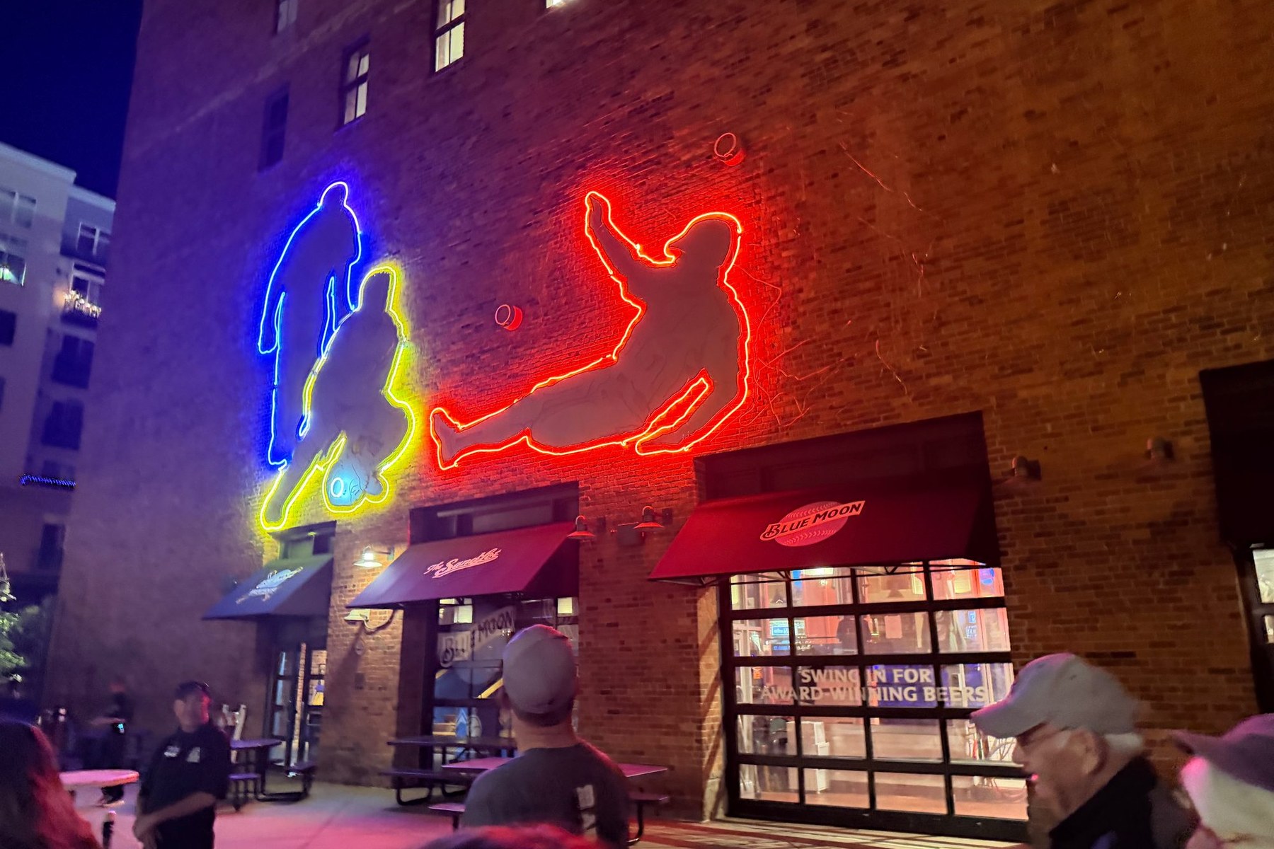 Neon bar signs glowing on an exposed-brick wall at a bar near Coors Field