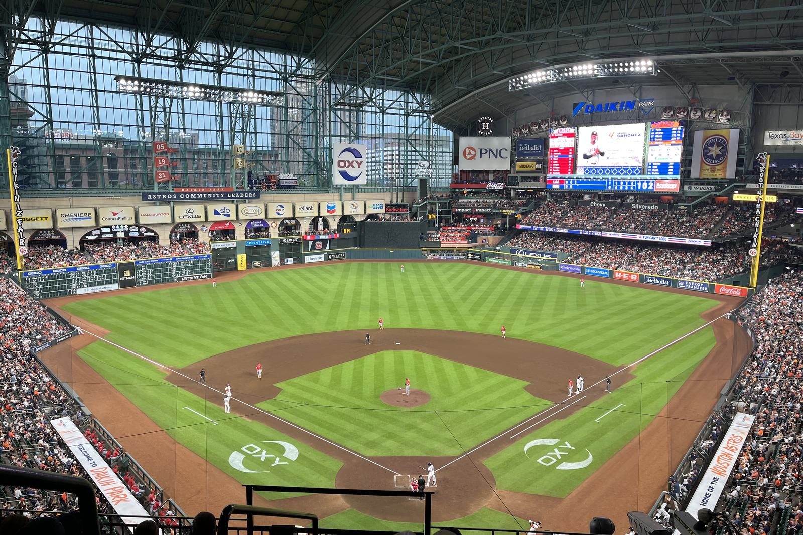 A full house at Daikin Park under the closed roof, the videoboard reading Daikin Park above the outfield and downtown Houston visible through the glass wall in left
