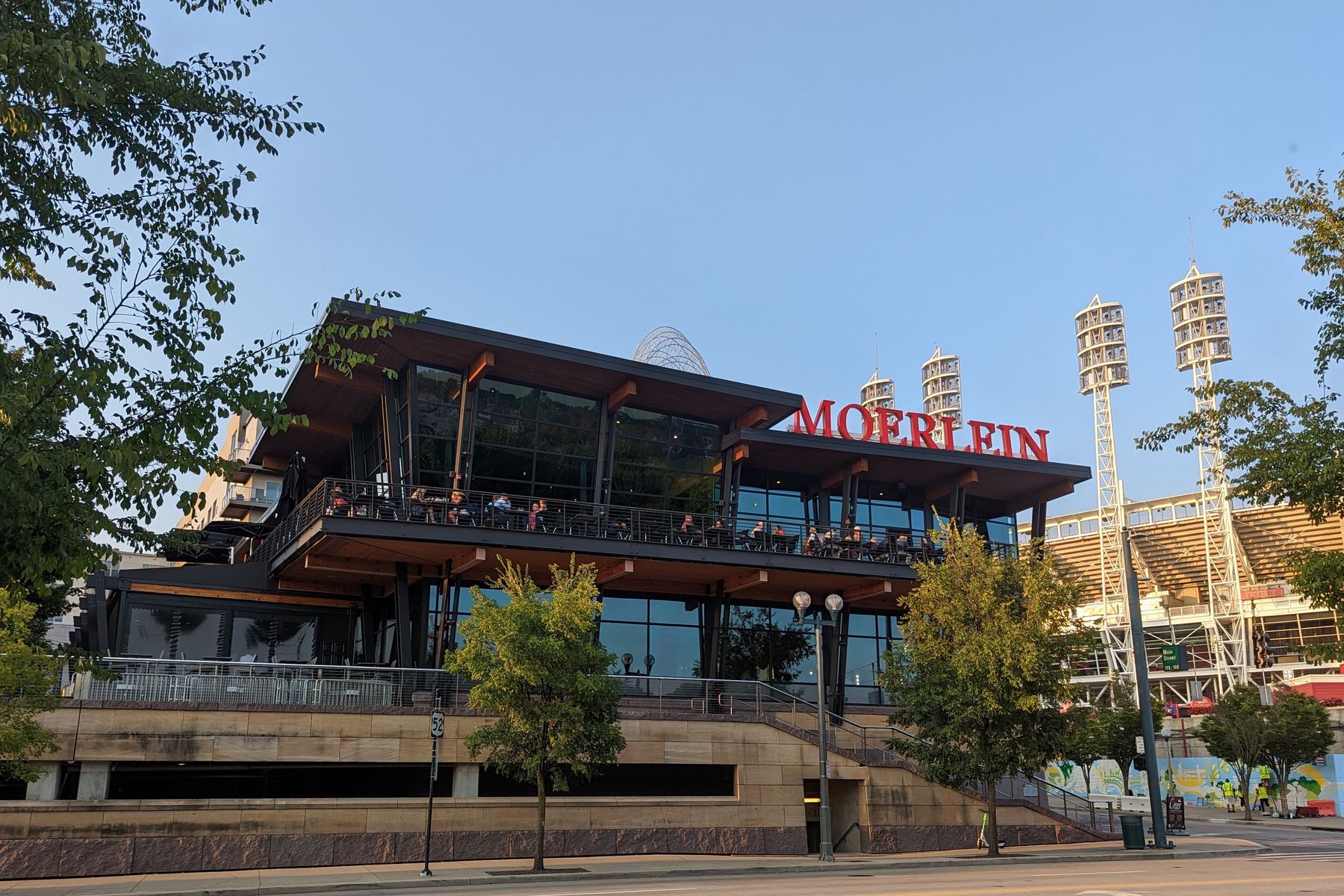 The Cincinnati Lager House (photographed under its former name, Moerlein Lager House) at dusk, its second-floor deck full of people, with the light towers and grandstand of Great American Ball Park rising directly behind it
