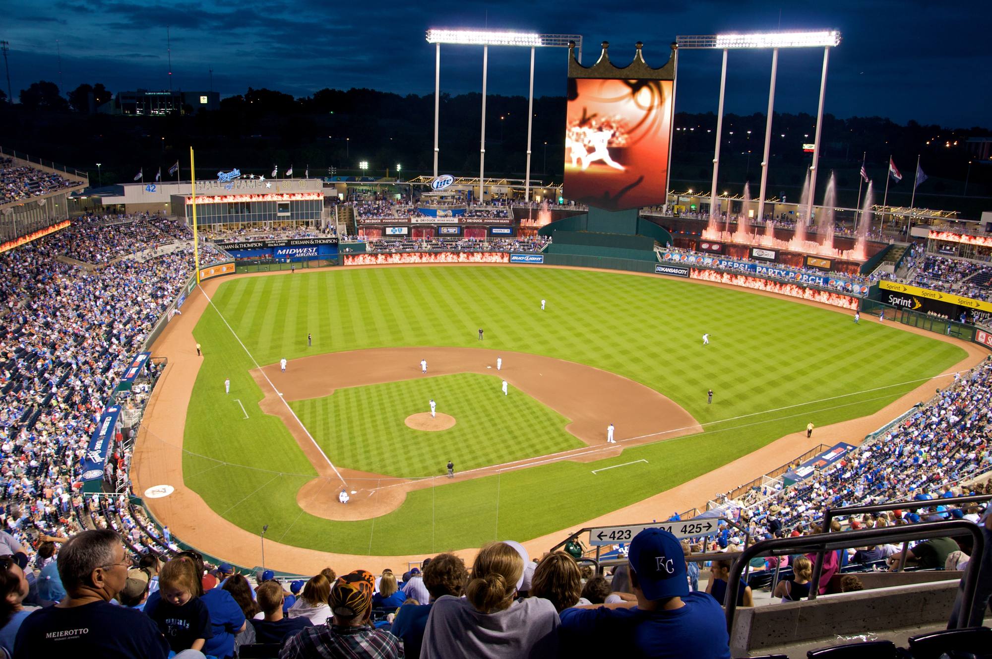 Kauffman Stadium at night with the crown scoreboard lit above center field and the bowl full