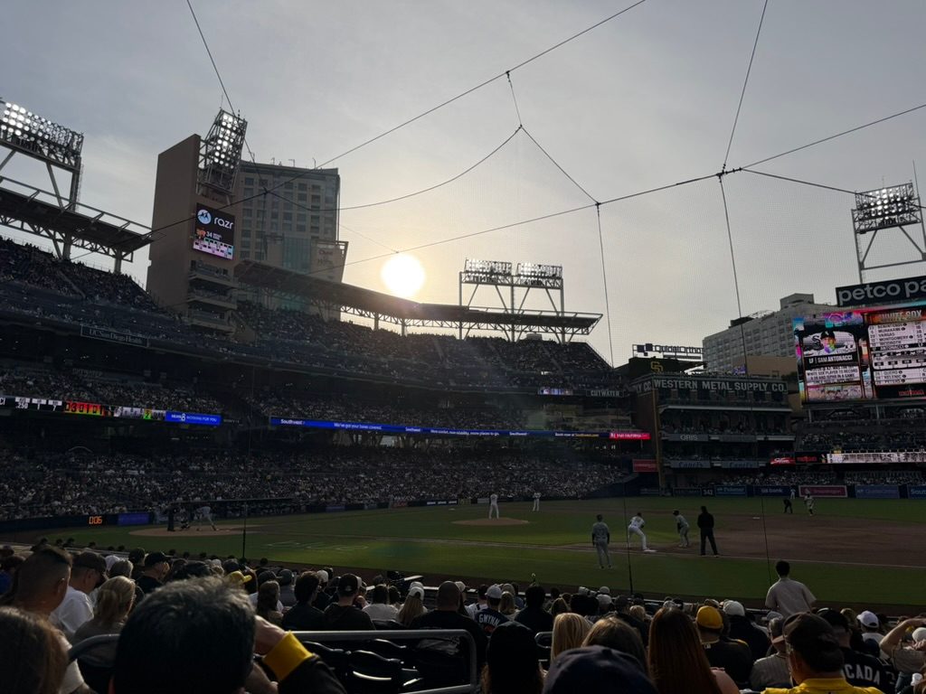 A lower-bowl view at Petco Park at sunset, with the Western Metal Supply Co. building and the sun setting over the third-base side beyond a full crowd