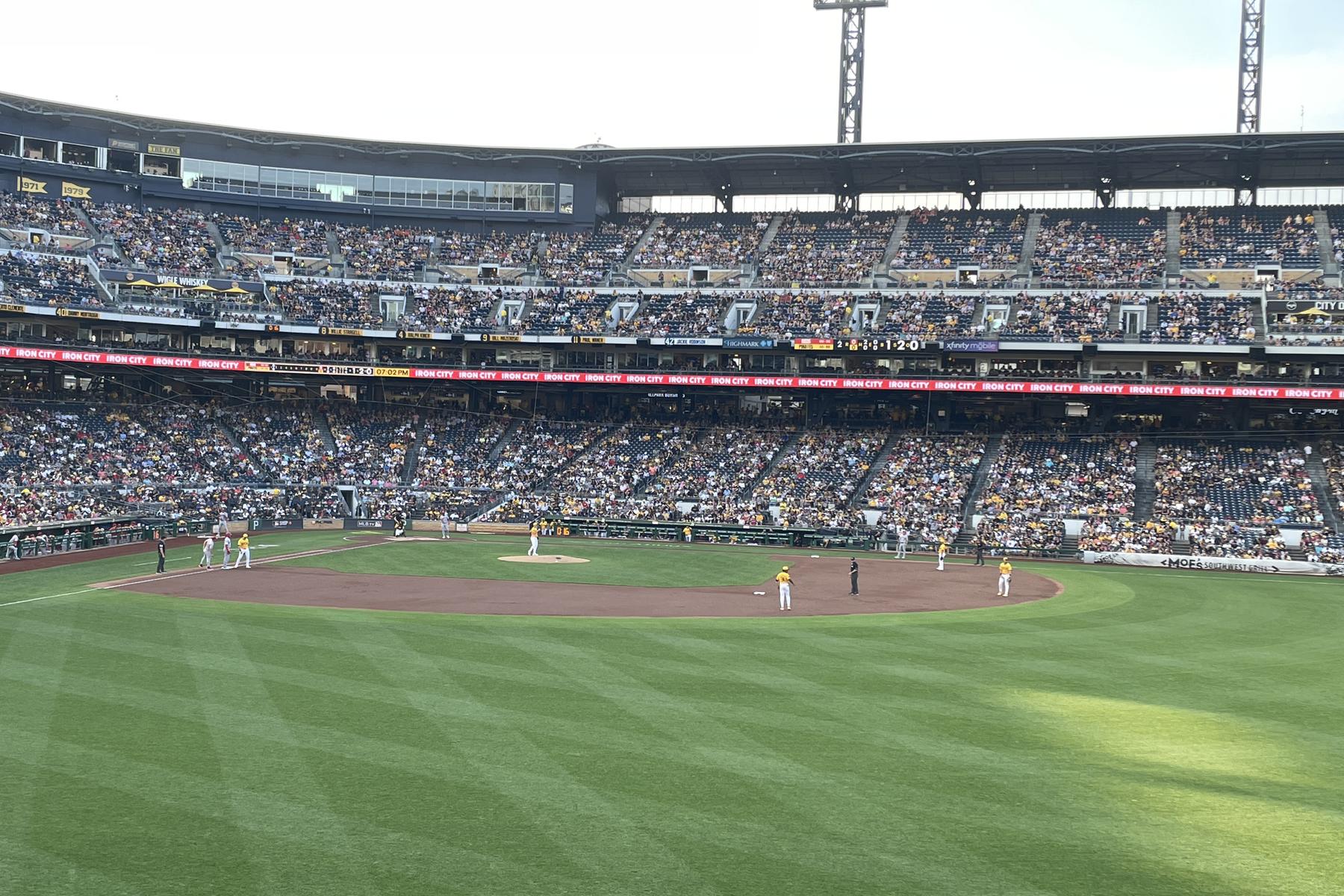 The packed grandstand at PNC Park seen from the outfield seats during a day game, the full seating bowl across the field