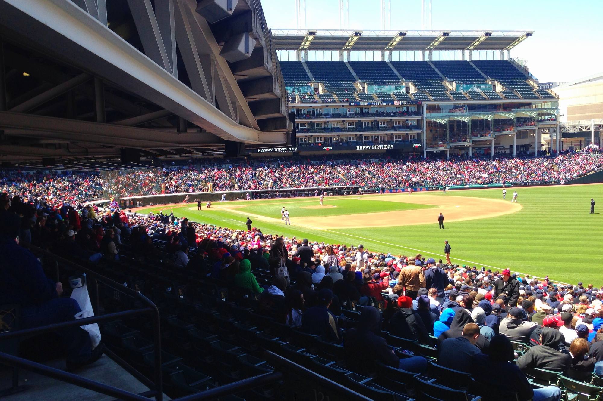 Fans filling the lower bowl at Progressive Field on a sunny afternoon, the infield and the upper deck in view from a seat down the line
