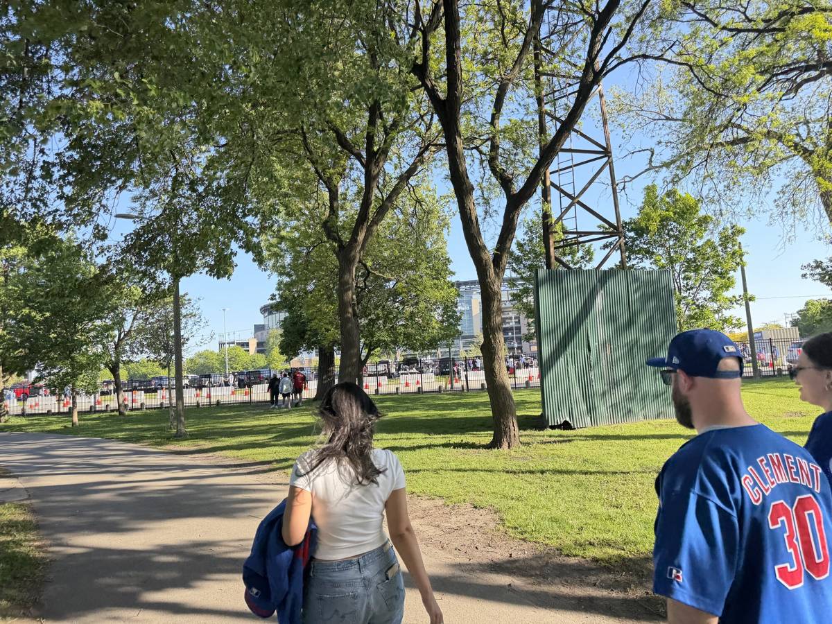 Sox fans walking through Armour Square Park toward Rate Field on a sunny afternoon, with the ballpark and team-operated parking visible in the distance