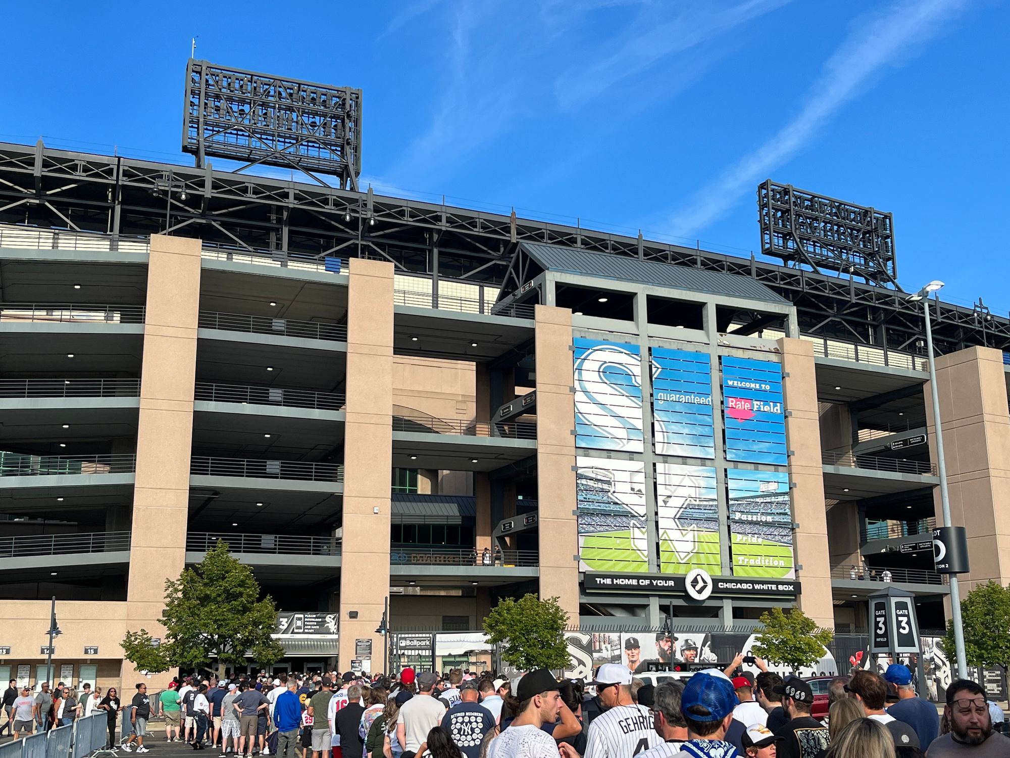 The exterior of Rate Field on a game day, with a crowd of fans gathered below the White Sox banner