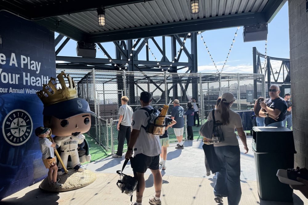 Fans walking into a covered batting cage area at T-Mobile Park past a large crowned Mariners figure