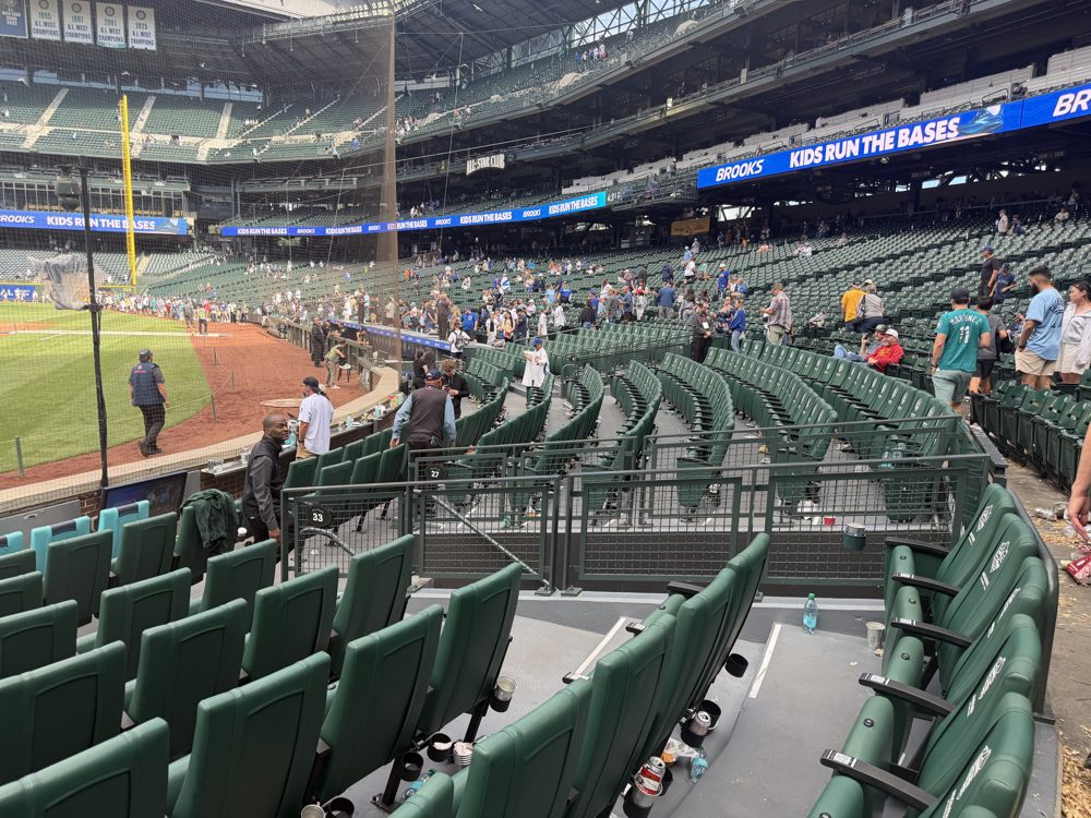 Empty padded green seats behind home plate at T-Mobile Park after the game, with section 33 and section 27 markers on the rail and a Kids Run the Bases banner above