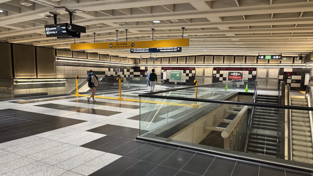 The mezzanine of a downtown Seattle Link light rail station, with Pay to Enter signs, arrival boards, and stairs down to the platform