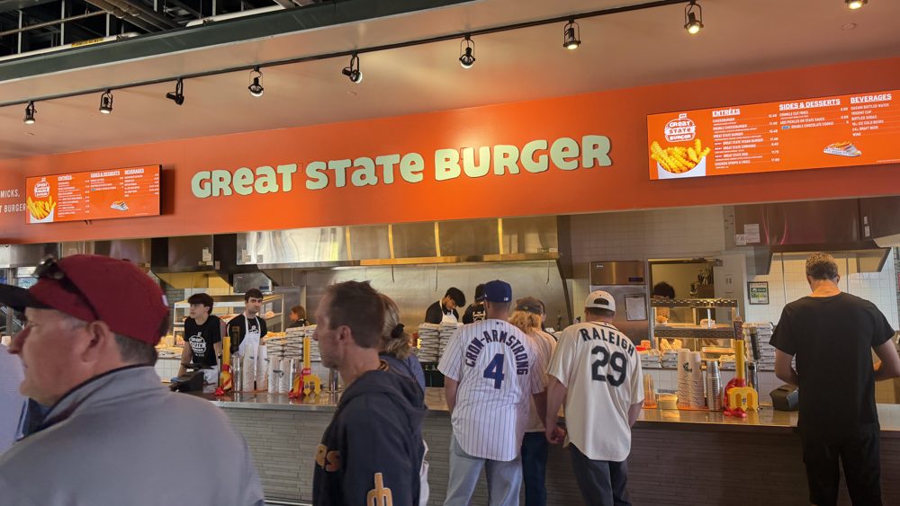 Fans in line at the Great State Burger stand at T-Mobile Park, its orange sign and lit menu boards over the counter