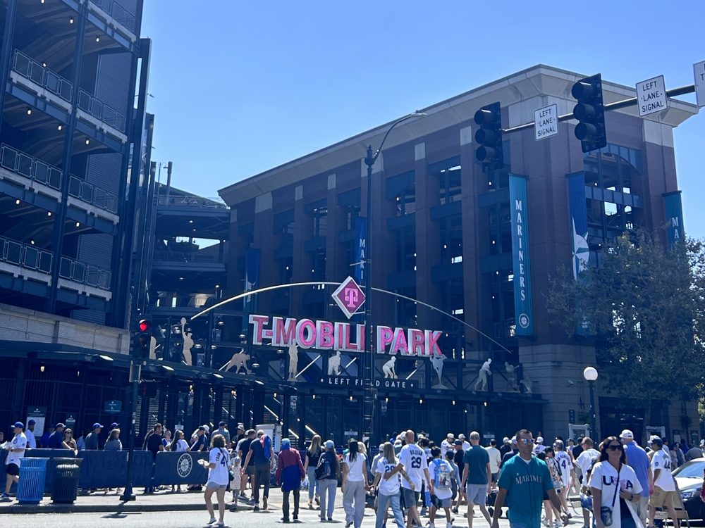 Fans crowding the street outside the Left Field Gate at T-Mobile Park, under the pink T-Mobile Park sign on a sunny day