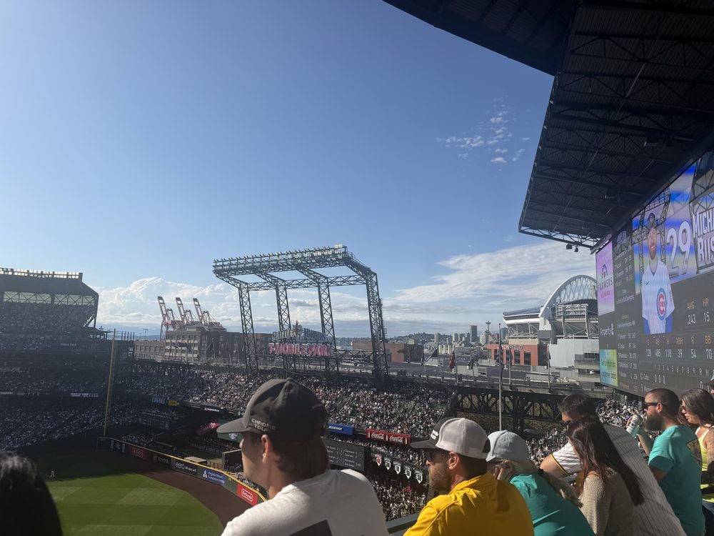 Fans at the top level of the stands in right field at T-Mobile Park, looking out over the outfield toward cargo cranes, the downtown Seattle skyline, and the roof of Lumen Field