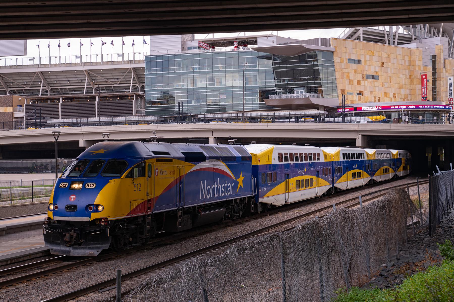 A Northstar commuter train stopped at the platform below Target Field, the ballpark's limestone facade rising behind it