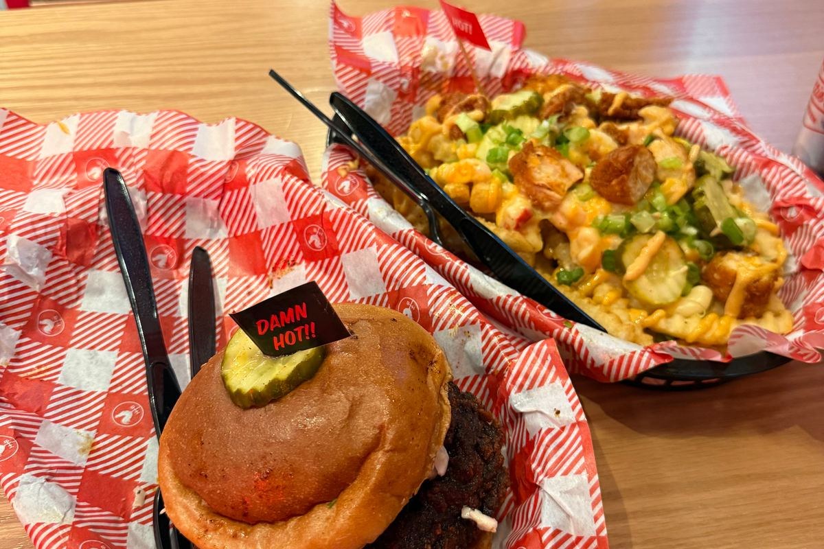 A smashburger topped with a pickle next to a basket of loaded fries in checkered paper at Wrigley Field