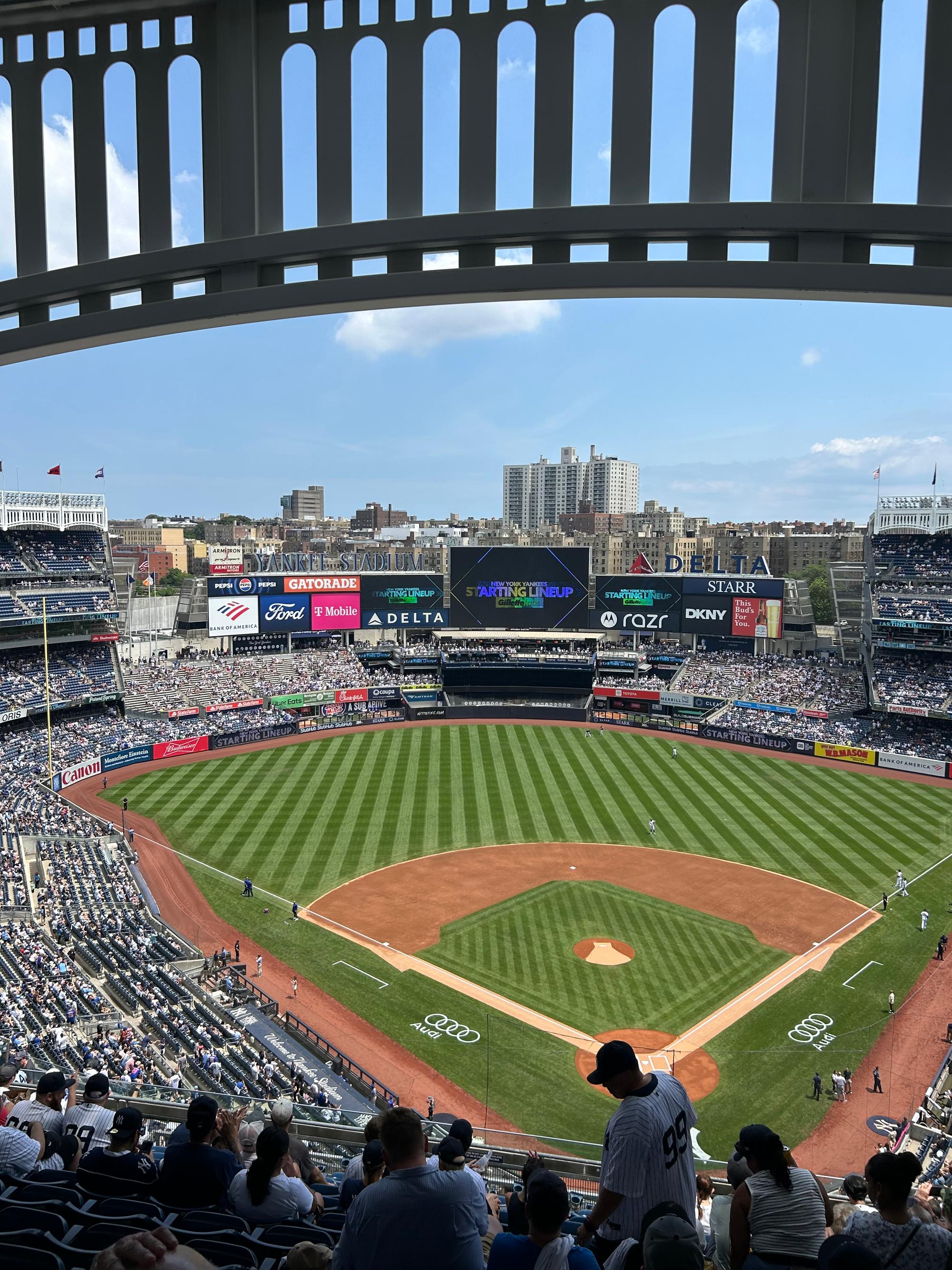 The view from the upper Grandstand behind home plate at Yankee Stadium, framed by the white frieze along the roof, with the videoboard and the Bronx apartment buildings beyond the outfield